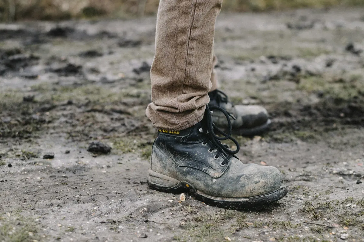 A well-worn, mud-caked boot standing on a damp dirt path